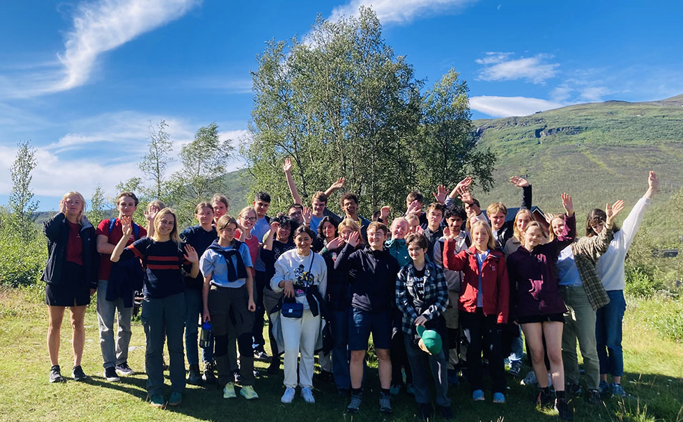 Bild: gruppfoto med ungdomar utomhus i fjällnatur, flera vinkar med uppsträckta armar