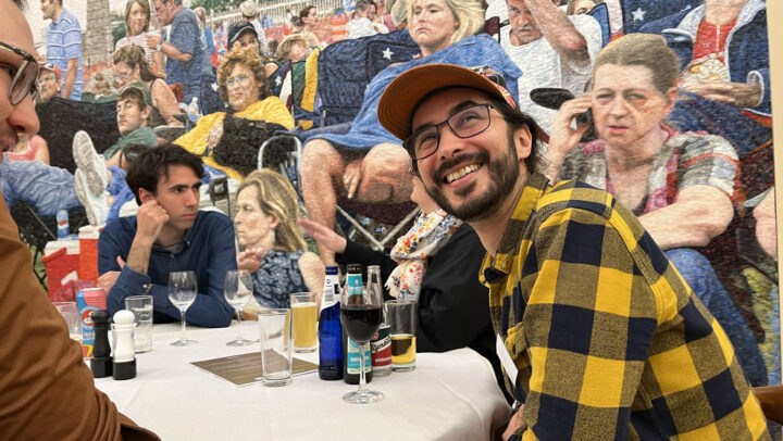 Bild: Juan Rocha sitter och ler upp mot någon, i fonden stor väggmosaik föreställande folksamling